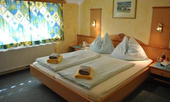 A cozy bedroom with a double bed and two pillows. The window is decorated with colorful curtains and there are towels on the bed.