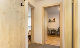 A bright entrance area with wooden details and several doors. In the background, comfortable seating and a decorative wall shelf can be seen.