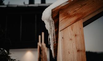 A wooden eaves with hanging icicles. In the background, a modern building is visible.