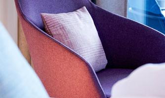 A modern armchair in purple and orange with a cushion. In the background, curtains and a window can be seen.