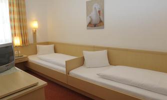 A simple room with two single beds and a cozy atmosphere. There is a window with curtains and a picture of a duck on the wall.