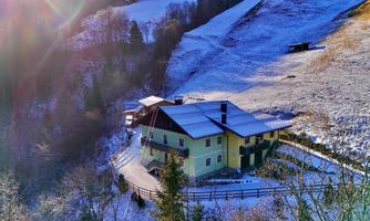 A picturesque house in the midst of a snow-covered landscape. The surroundings are characterized by trees and gentle hills.