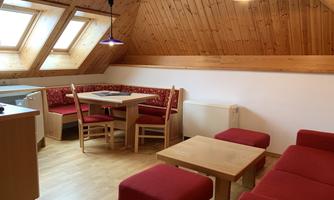 A cozy room with wooden walls and a table with chairs. Red seating furniture and large windows let in plenty of light.