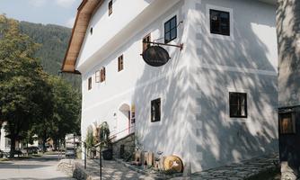 A pretty, white building with windows and a hanging sign. Surrounded by trees and a quiet village square.