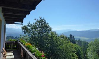 A viewing balcony with a view of green hills and mountains. The landscape is surrounded by trees and colorful flowers.