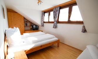 A cozy bedroom with wooden furniture and large windows. The room has a double bed and a television.