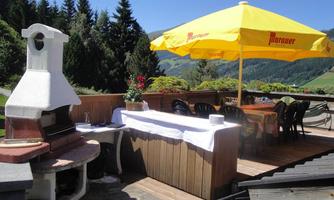 A cozy outdoor area with a grill and table under a yellow umbrella. The view of the green landscape and the trees creates an inviting atmosphere.