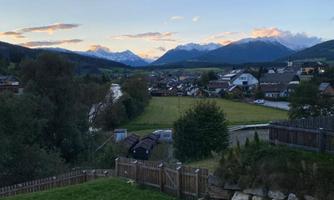 A picturesque landscape with mountains in the background and a quiet village. The sky is blue with some clouds.