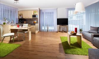 A modern living room with a dining area and an open kitchen. The space is bright and cheerful, with green carpets and large windows.