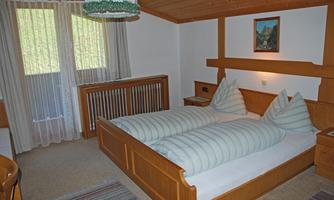 A cozy bedroom with a large wooden bed and two pillows. The walls are light, and a window lets in plenty of light.