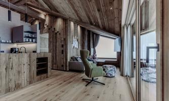 A modern, cozy living room with wooden walls and large windows. The decor is stylish and inviting, with a comfortable seating area and an open kitchen.