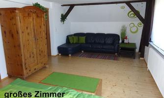 A large room with an old pine cabinet and dark wooden components. A green couch and a light wooden floor complete the cozy atmosphere.