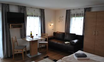 A cozy room with a sofa, a table, and two chairs. Large windows provide plenty of daylight and a welcoming atmosphere.