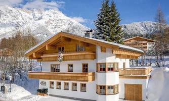 A cozy wooden house in the snow with a stunning mountain panorama in the background. The tranquil winter landscape offers a peaceful atmosphere.