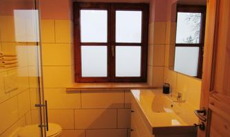 A modern bathroom with a bright tile design. There is a shower, a sink, and large windows.