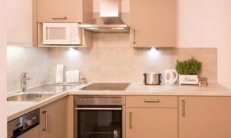 A modern kitchen with bright cabinets and stainless steel appliances. It is functional and well-equipped with a cooktop and sink.