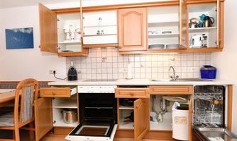 A cozy kitchen with wooden furniture and open cabinets. The stove and the dishwasher are visible, while the table is set for dining.