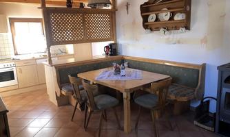 A cozy kitchen with a wooden dining area and a seating corner. Plates hang on the wall and the room has a warm, inviting atmosphere.