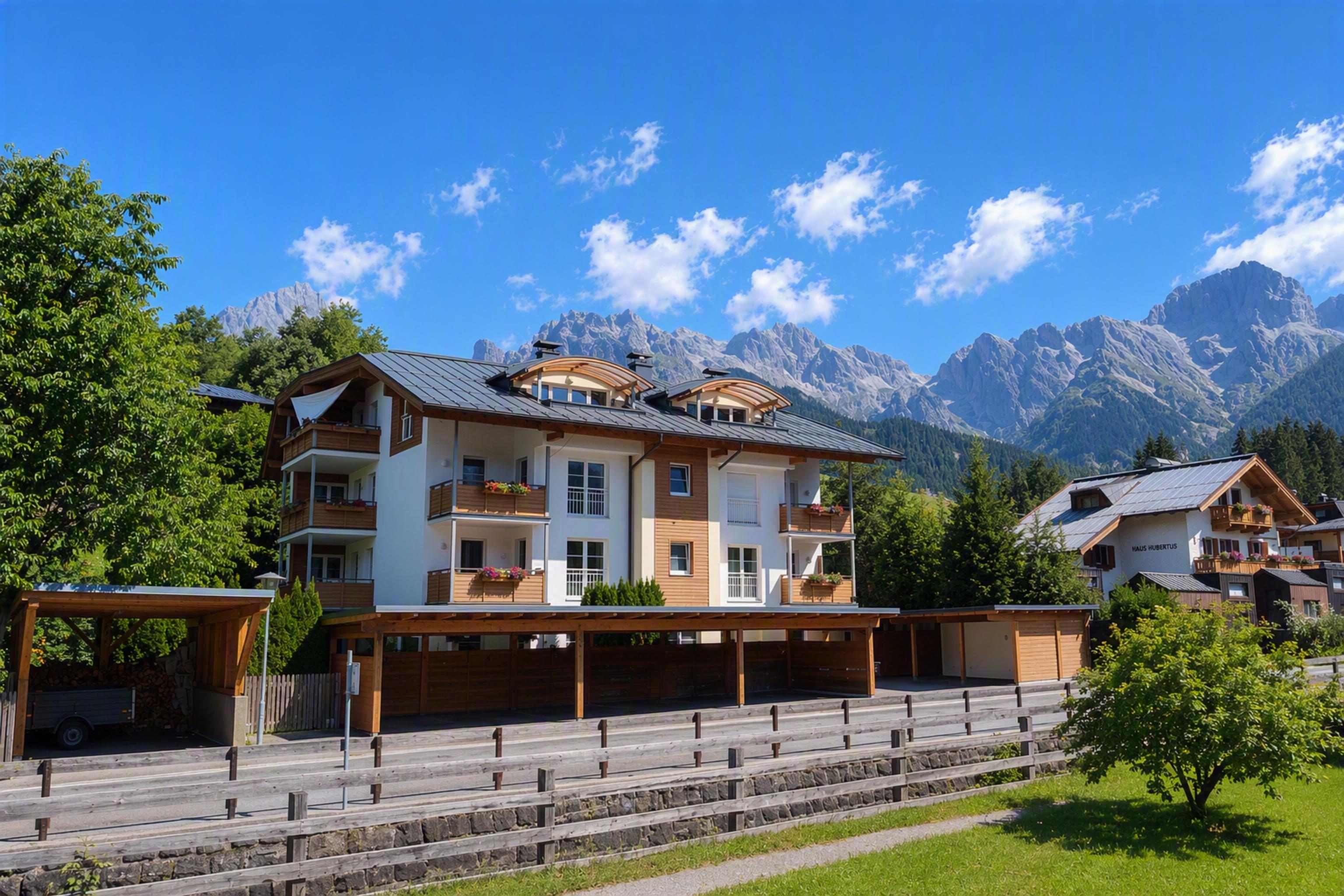 A modern building with balconies and a clear blue sky in the background. The surrounding mountains and trees give the scene a beautiful alpine atmosphere.
