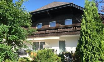 A charming house with wood siding and a balcony. Surrounded by trees and well-kept greenery.