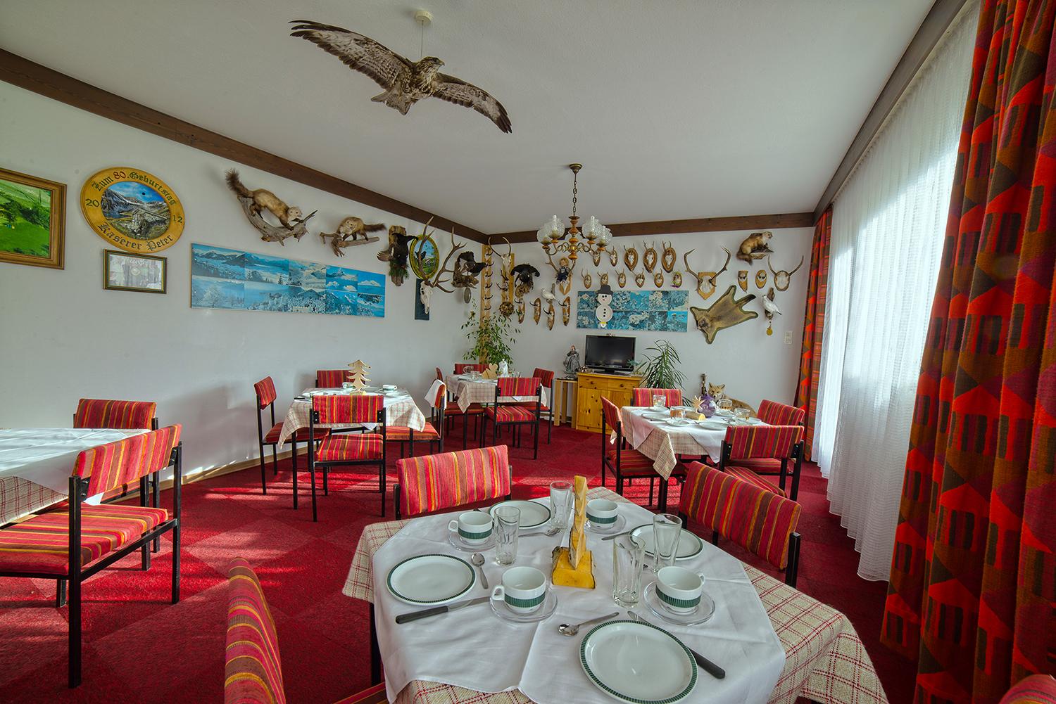 A cozy restaurant with red carpets and wooden tables. The walls are adorned with hunting trophies and decorative pictures.