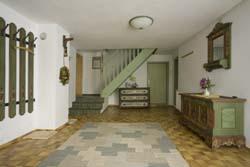 A bright entrance area with a staircase, green walls, and wooden furniture. The floor is covered with a carpet in various colors.