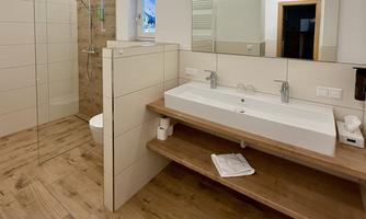 A modern bathroom with a walk-in shower and double sink. The wooden floor and neutral colors create a cozy atmosphere.