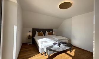 A modern bedroom with a large bed and wooden floor. There are two nightstands with lamps and plenty of natural light.
