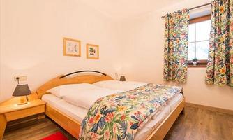 A cozy bedroom with a large bed and colorful floral patterns. There are wood details and a warm tone in the decor.