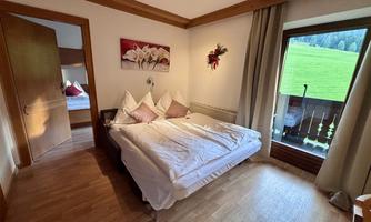 A cozy bedroom with a double bed and two pillows. The room has large windows overlooking a green meadow.