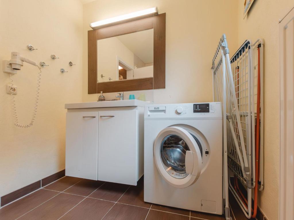 <p>Laundry room with washing machine, sink with mirror cabinet and a folded clothes dryer on the wall – all on brown tiled floor.</p>