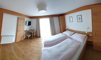 A bright bedroom with two single beds and wooden decor. There is a small table, a television, and access to the terrace.