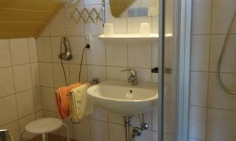A small bathroom with a shower, sink, and toilet. Towels and a stool are also available.