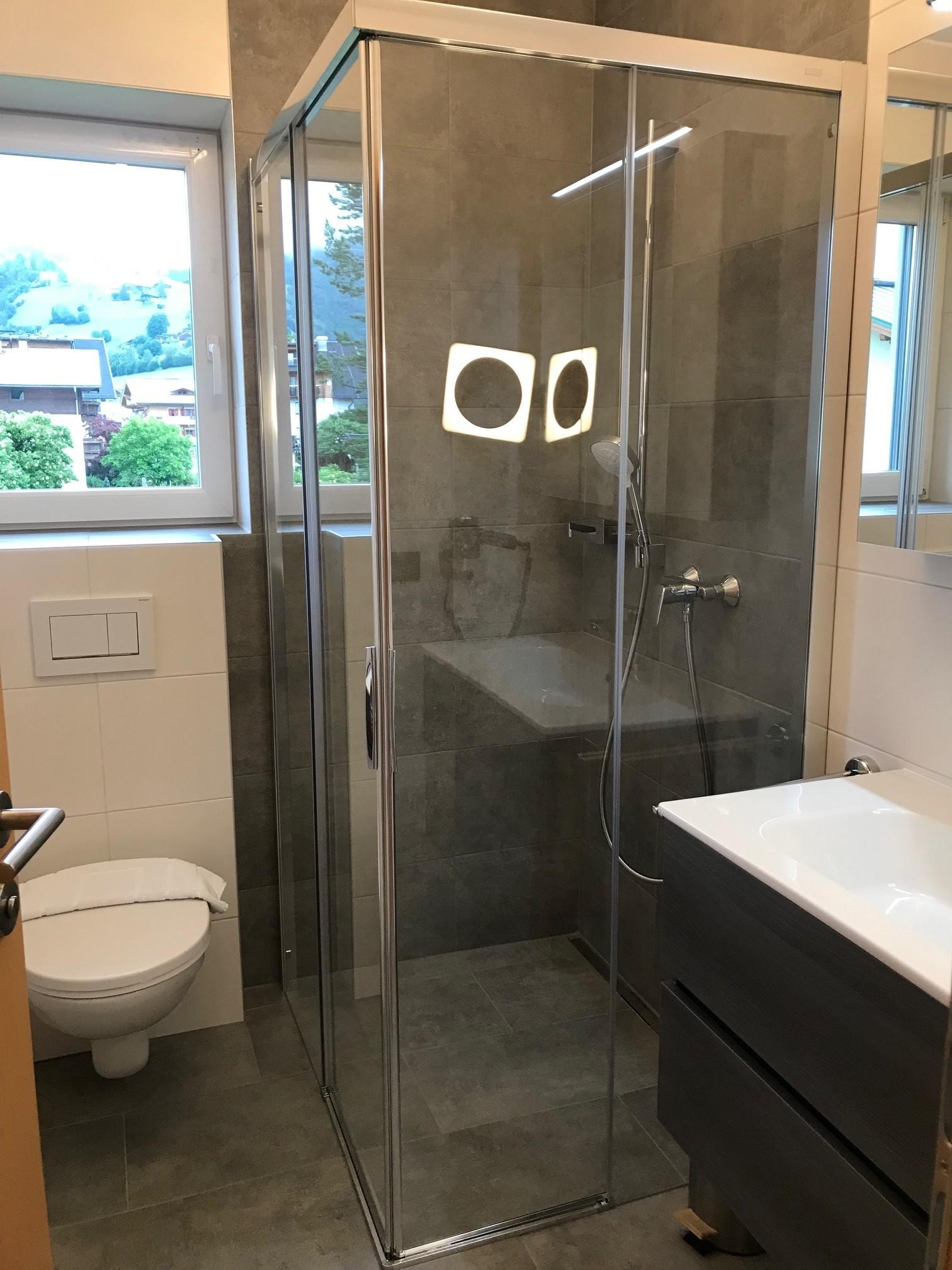 A modern bathroom with a glass shower and a sink. There is a window that provides light and a view.