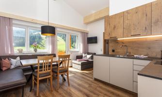 A modern kitchen with dining table and wood paneling. Large windows provide plenty of natural light and a view of nature.
