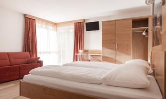 A modern room with a double bed and a red sofa. Large windows let in plenty of light and create a friendly atmosphere.