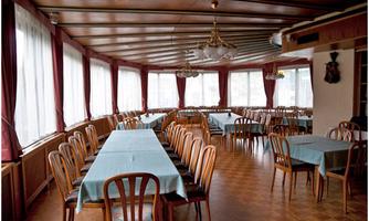 A large, bright dining room with several tables and chairs. The windows are adorned with curtains and let in plenty of light.