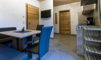 A modern kitchen with a dining area, equipped with a table and chairs. The walls are light, and there are wooden details for decoration.