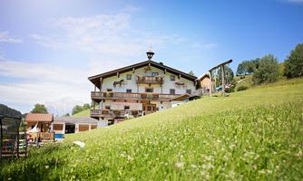 A charming country house surrounded by lush greenery and blue sky. Gentle hills are visible in the background.