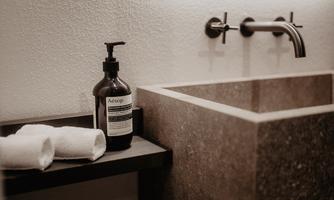 An elegant stone sink with a modern faucet. Next to the sink are two towels and a bottle of liquid soap.