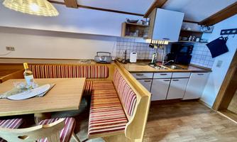 A cozy kitchen with a dining area and a comfortable seating area. The furniture has a rustic wood look and there are modern kitchen appliances.