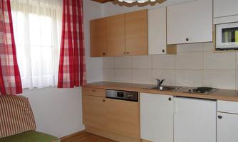 A cozy kitchen with wooden cabinets and a modern stove.  
Red curtains and a comfortable sofa create an inviting atmosphere.
