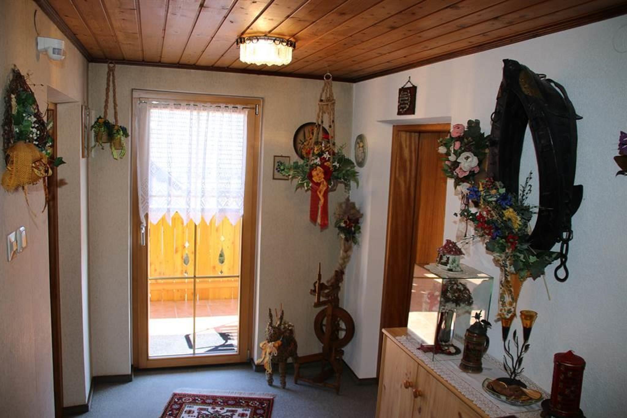 A cozy hallway with a wooden ceiling and decorative flower arrangements. Through the door, a balcony with a railing is visible.
