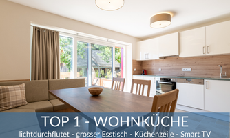 A bright living kitchen with a large dining table and modern kitchen equipment. The large windows provide plenty of daylight and a view of the outside.