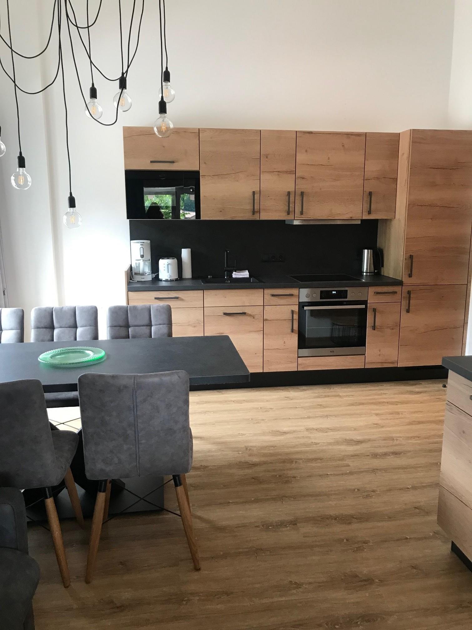 A modern kitchen with wooden cabinets and an elegant kitchen unit. In the foreground, there is a dining area with gray chairs.