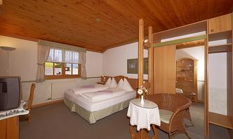 A bright and cozy hotel room with a wooden ceiling. There is a double bed, a small table, and a wardrobe.