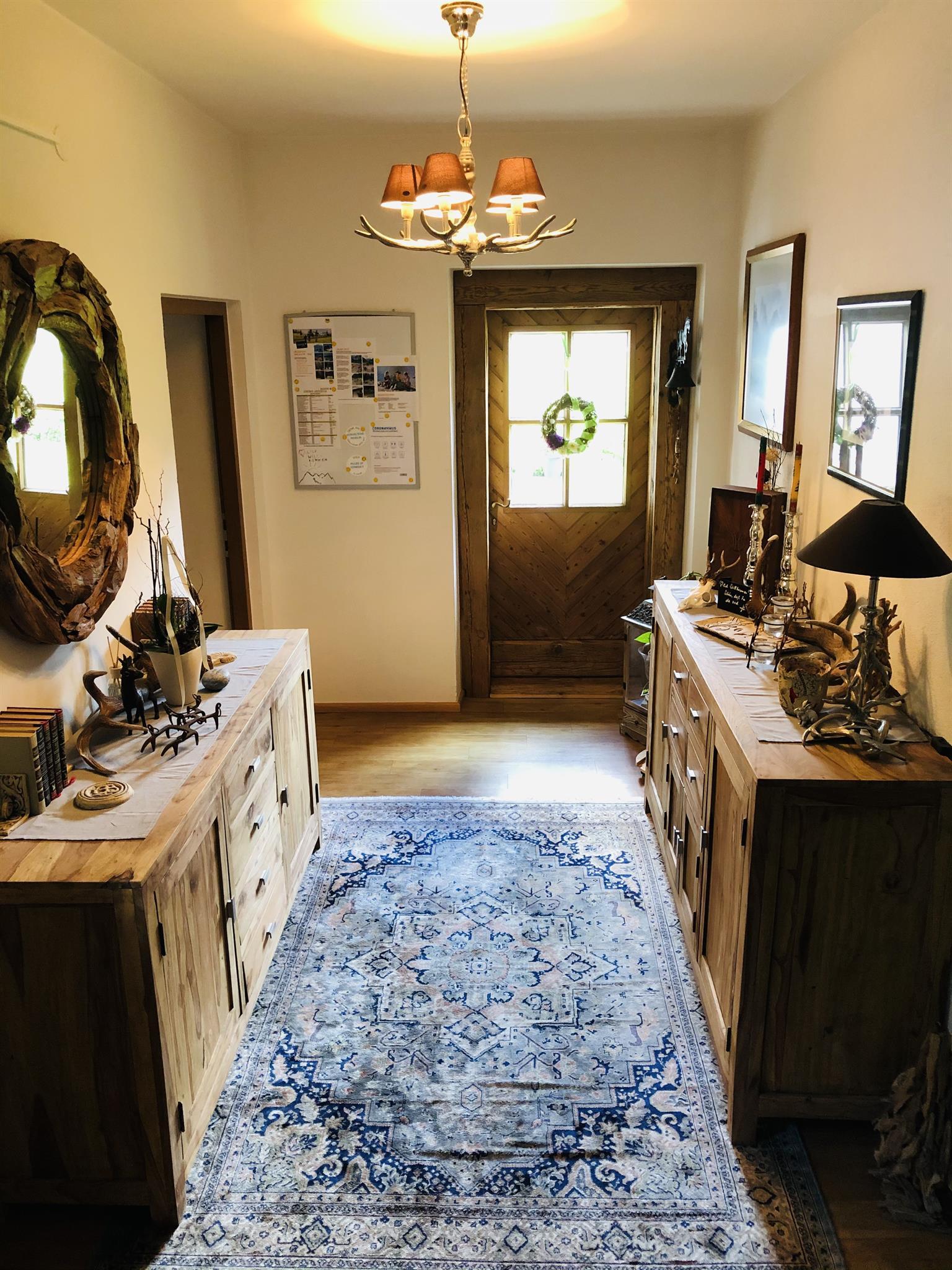 An inviting hallway with wooden furniture and a beautiful rug. Pictures hang on the wall and a door with a decorative wreath.
