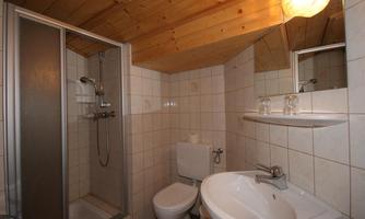 A small bathroom with a shower, a sink, and a toilet. The walls are tiled, and the ceiling is made of wood.