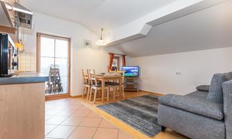 A bright and modern kitchen-living room with a dining table and a cozy sofa. Generous windows provide plenty of daylight.