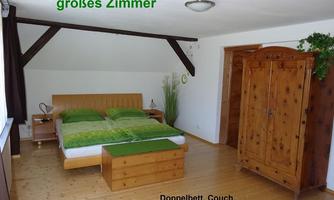 A large room with a double bed and a sofa. The dark wooden beams and the colorful lights create a cozy atmosphere.